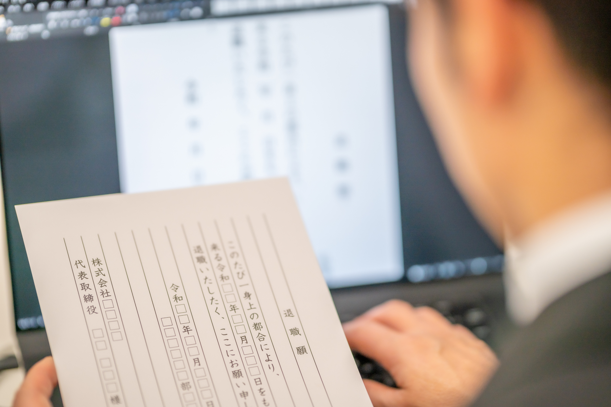 退職届の見本を見て退職届を作成している男性